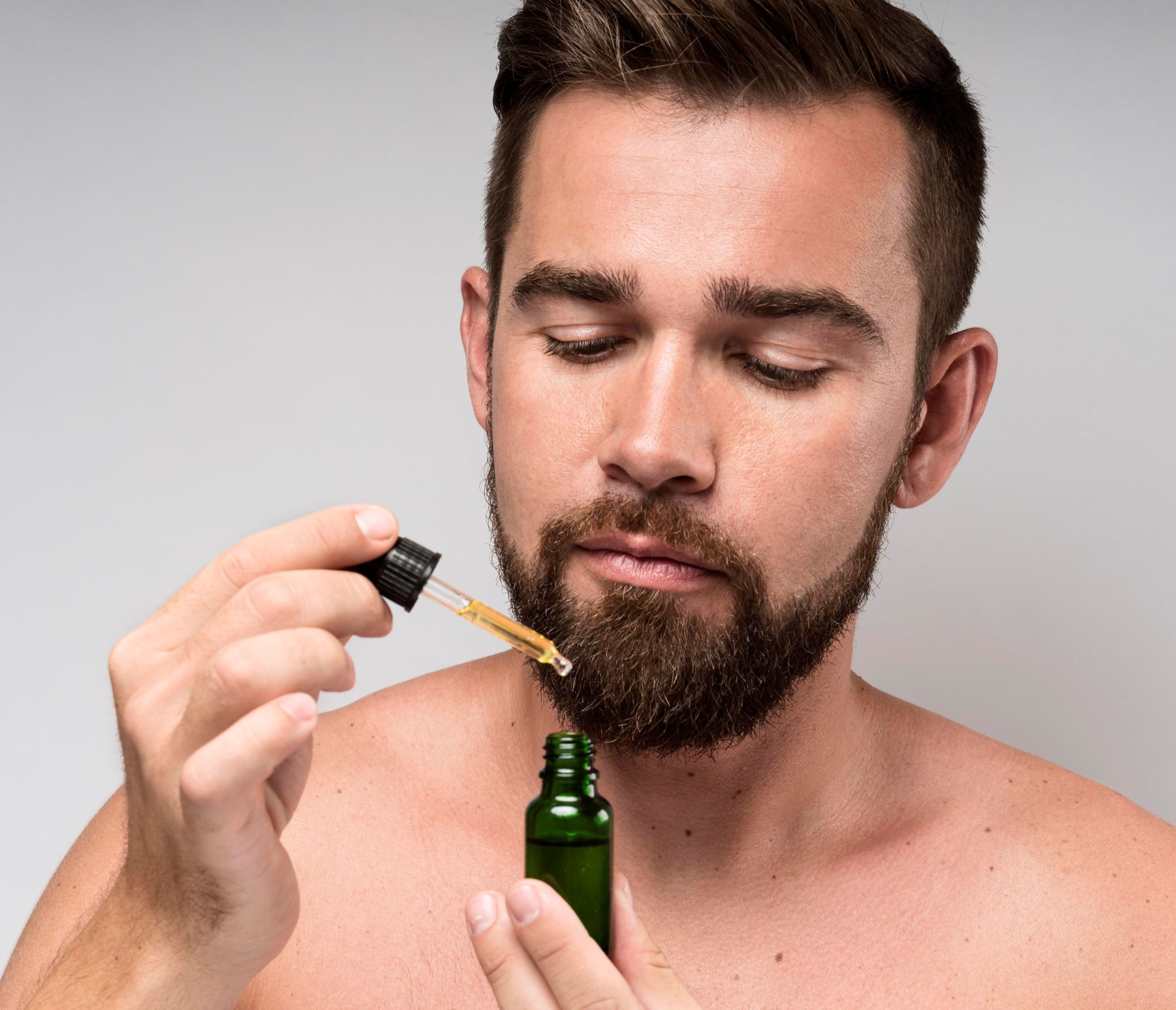 Man holding hair oil in green bottle, with pipette
