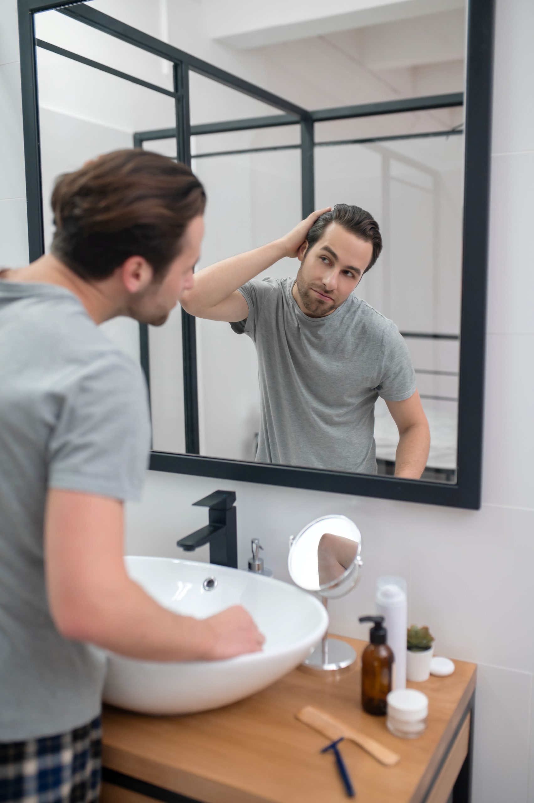 Man in grey Tee-shirt checking his hairline in a mirror
