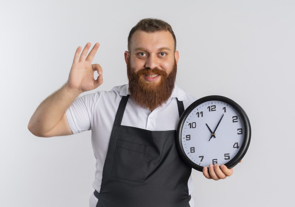 Bearded professional barber in apron showing the best time to cut your hair