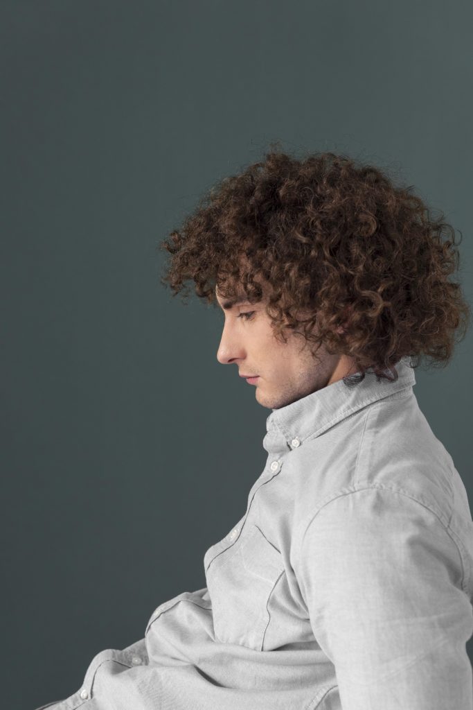 Curly-haired young man in collared shirt, sitting against a background