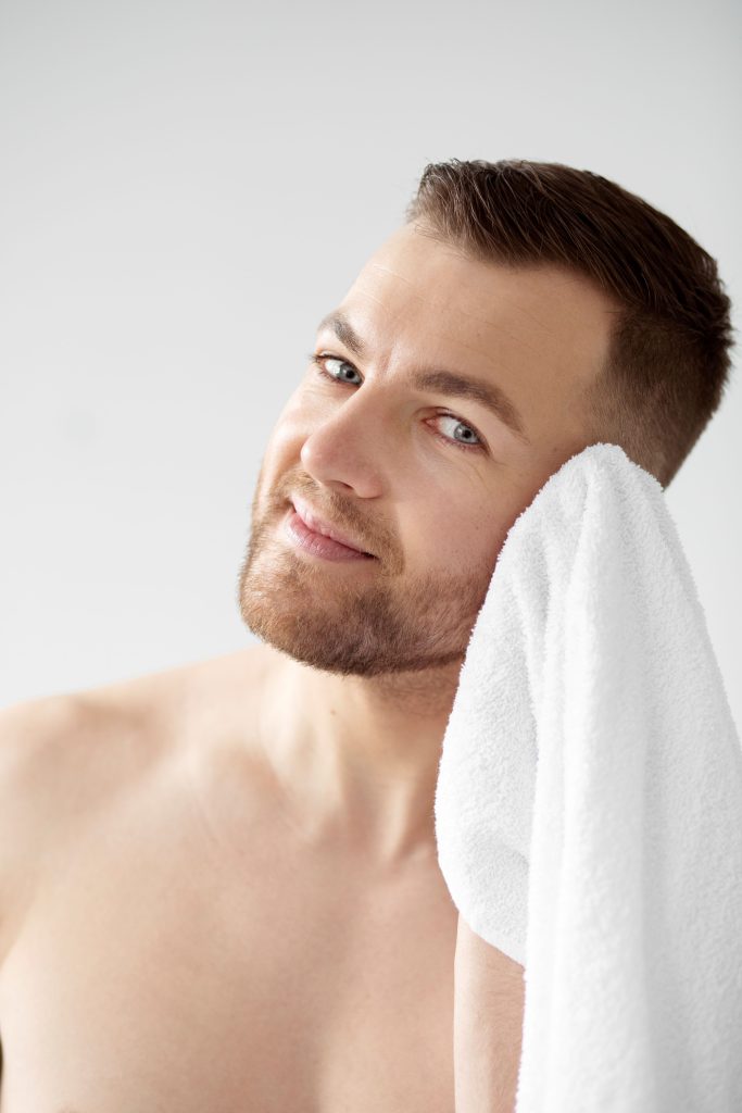 Young man with short hair gently patting wet hair dry with microfiber towel demonstrating proper hair drying technique