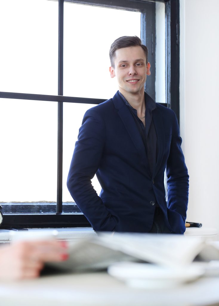 Confident man with attractive hairstyle, wearing dark-colored suit and smiling in an office.